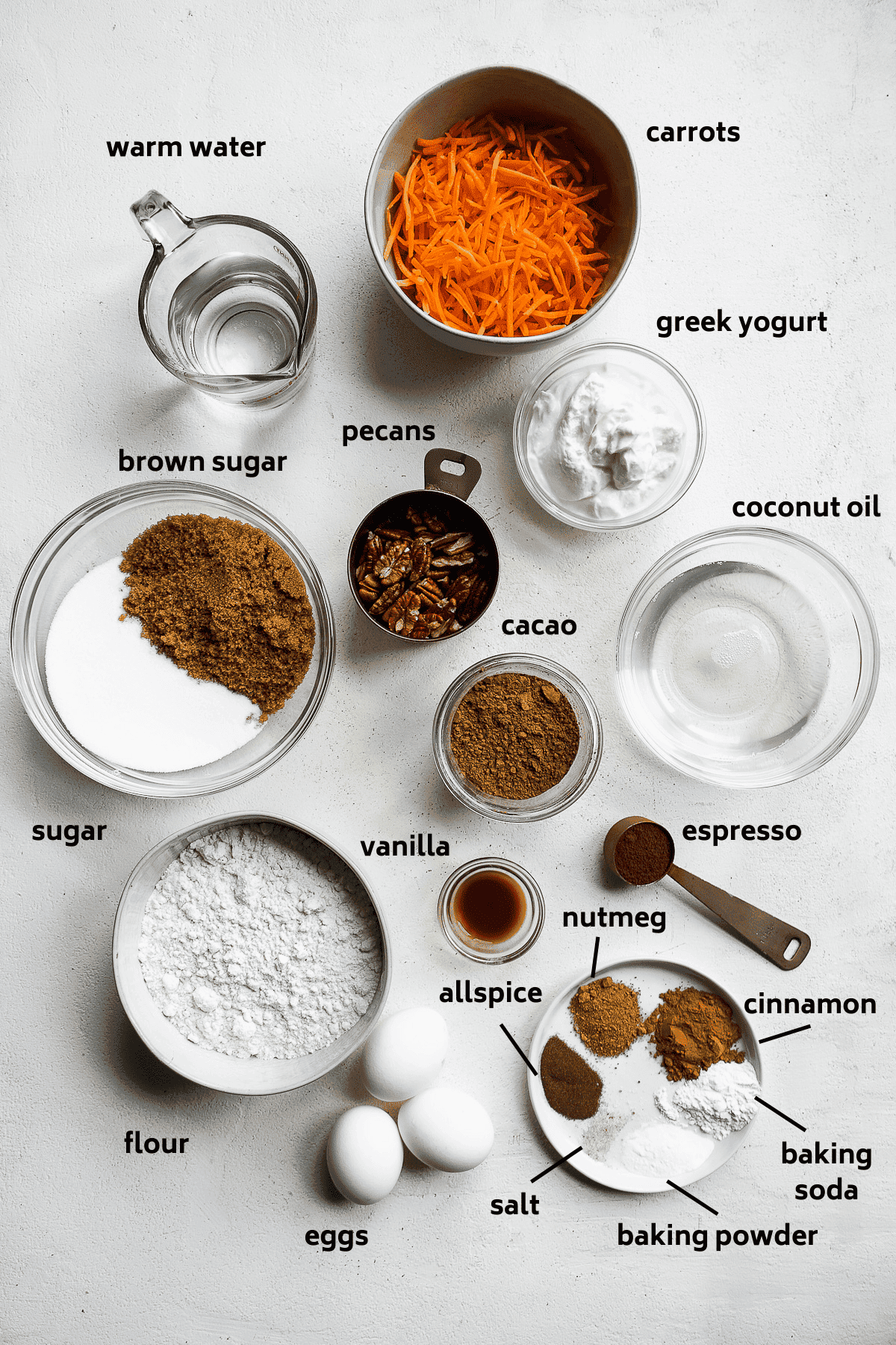 Chocolate carrot cake ingredients on a white surface with labels in black.