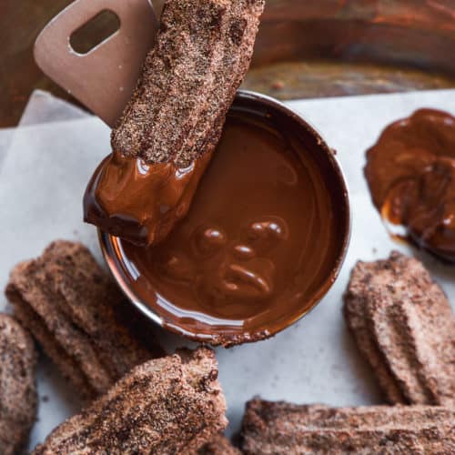 Chocolate churros scattered on white parchment paper and dipped in chocolate.
