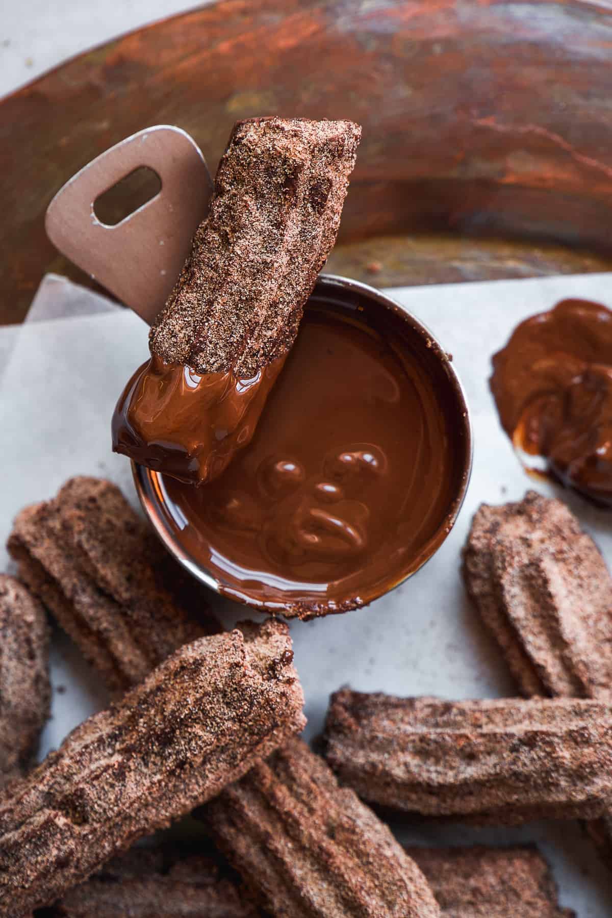 Chocolate churros with chocolate dipping sauce on a copper platter.