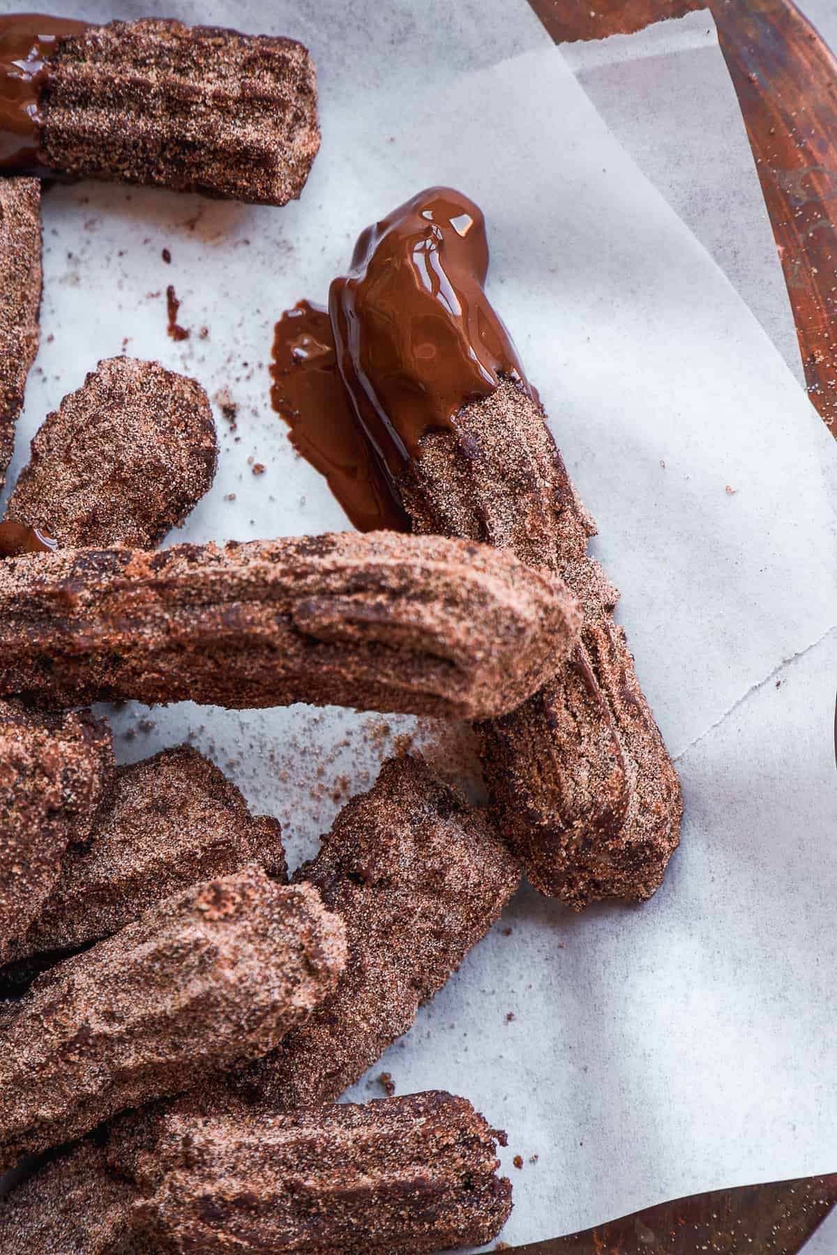 Chocolate churros dipped in chocolate on white parchment paper.