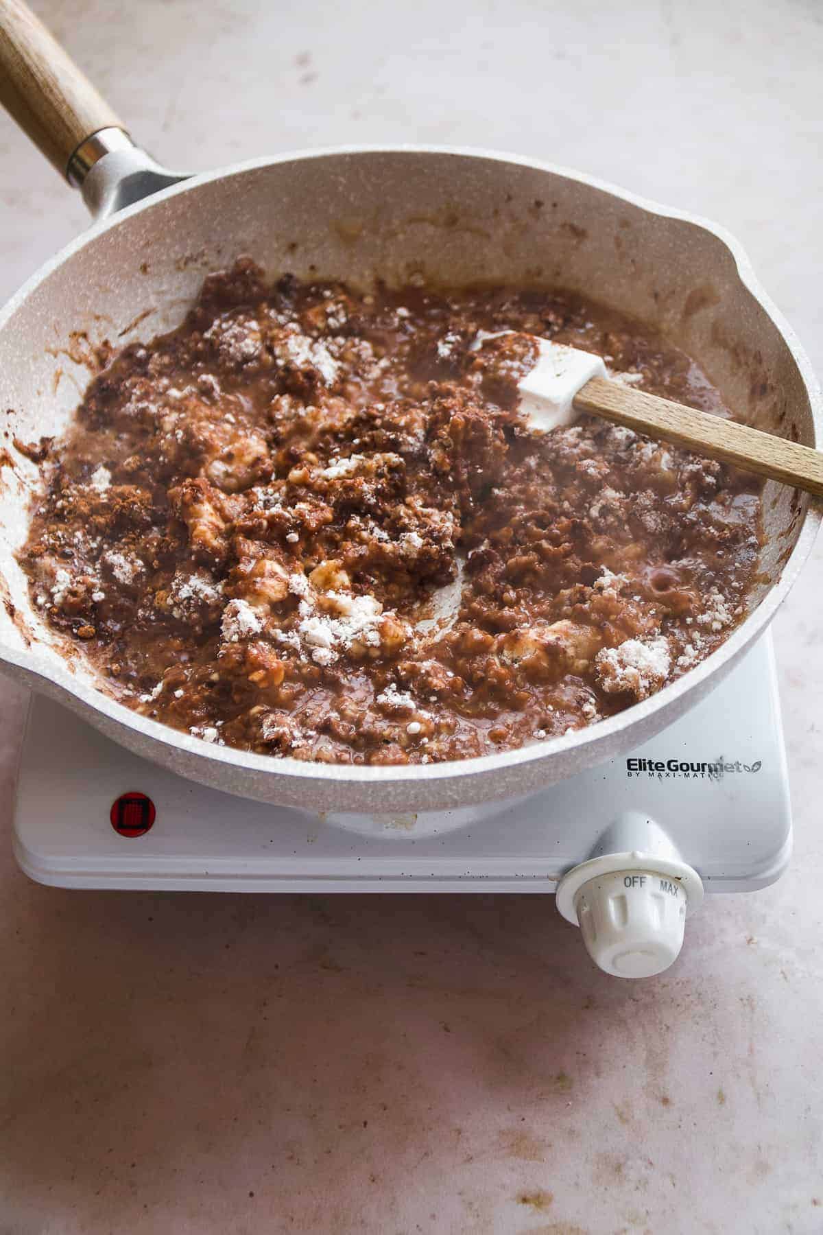 Gray skillet with chocolate and flour mixture being stirred with a spatula.