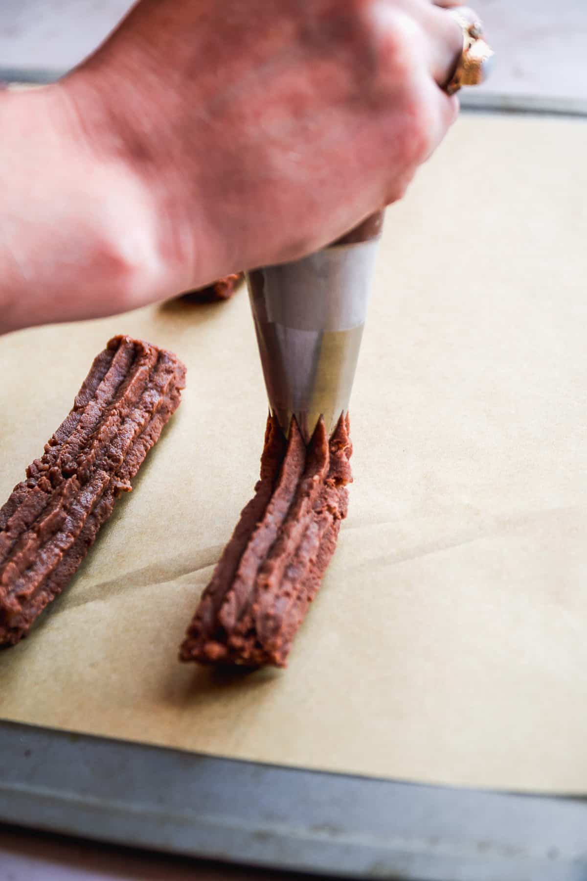 Person piping a churro onto a baking sheet with parchment paper.