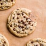 Oat flour chocolate chip cookies on brown parchment paper with a bite taken out of one.