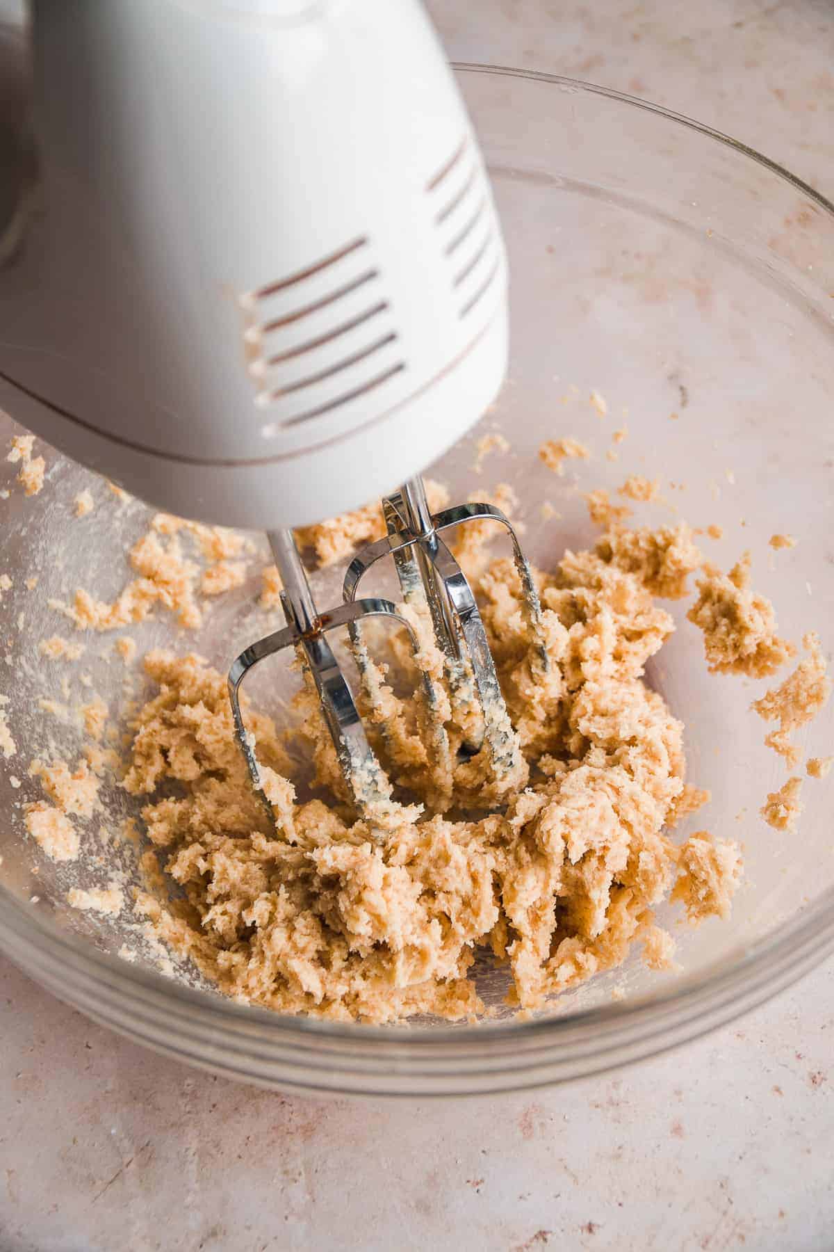 Mixer beating butter with sugar in a clear bowl.