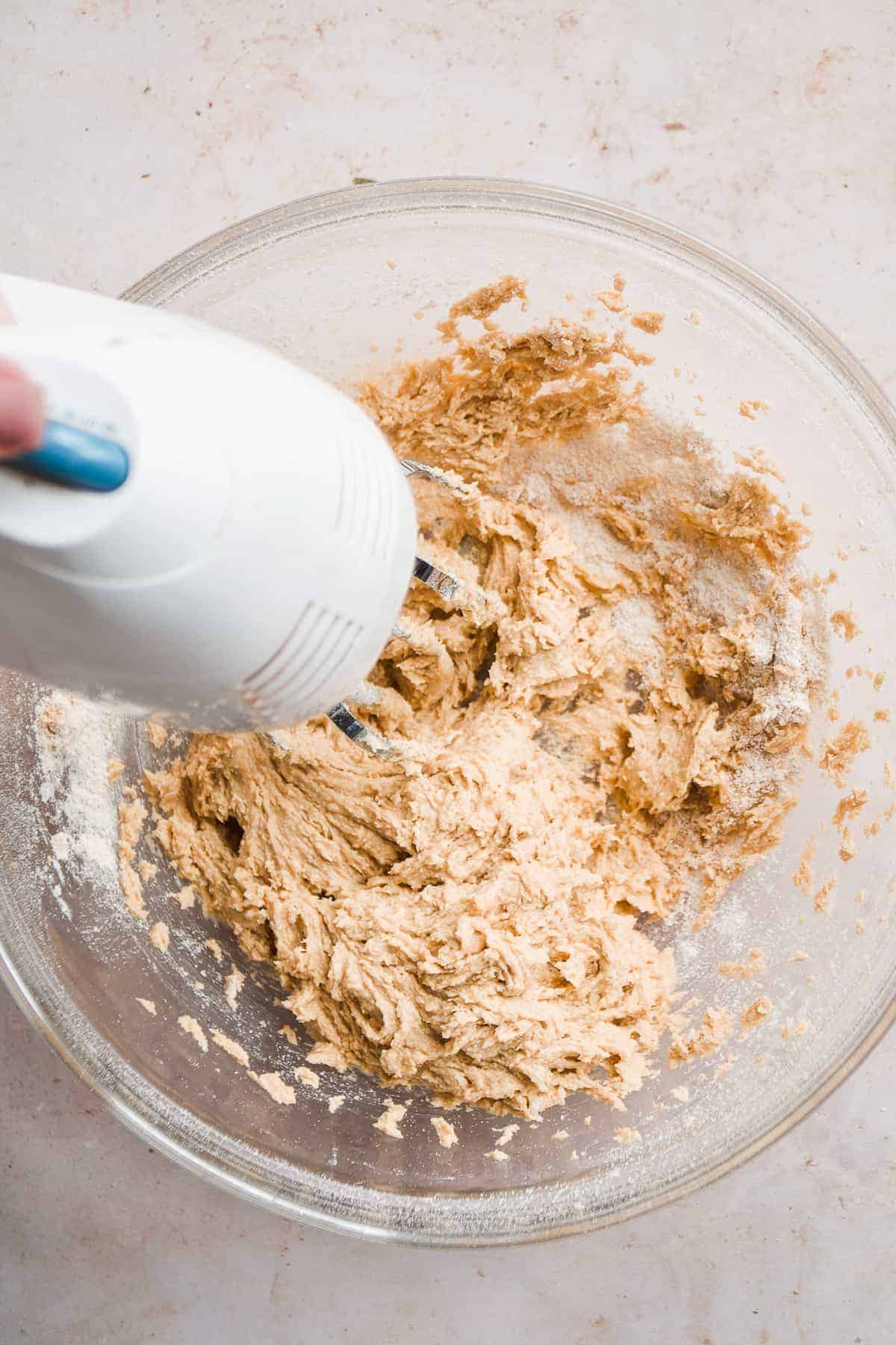 Overhead view of a mixer mixing cookie dough in a clear bowl.