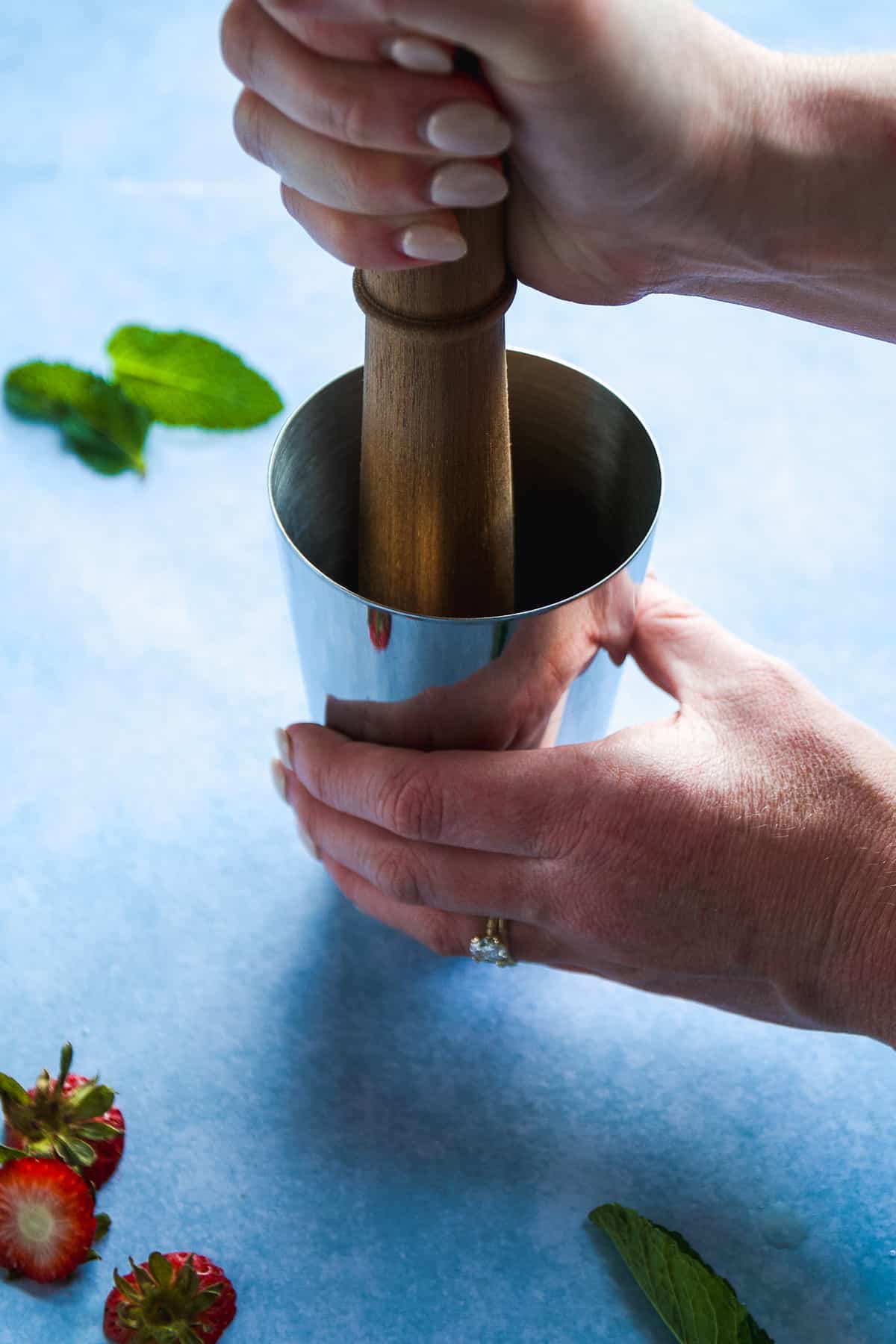 Person muddling strawberries in the bottom of a cocktail shaker.
