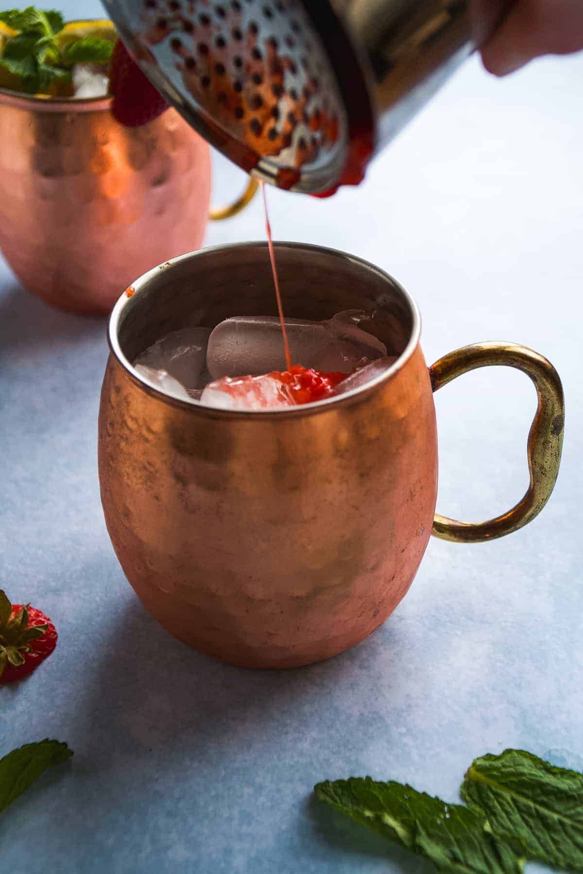 Person pouring the strawberry puree into a copper mug with ice.