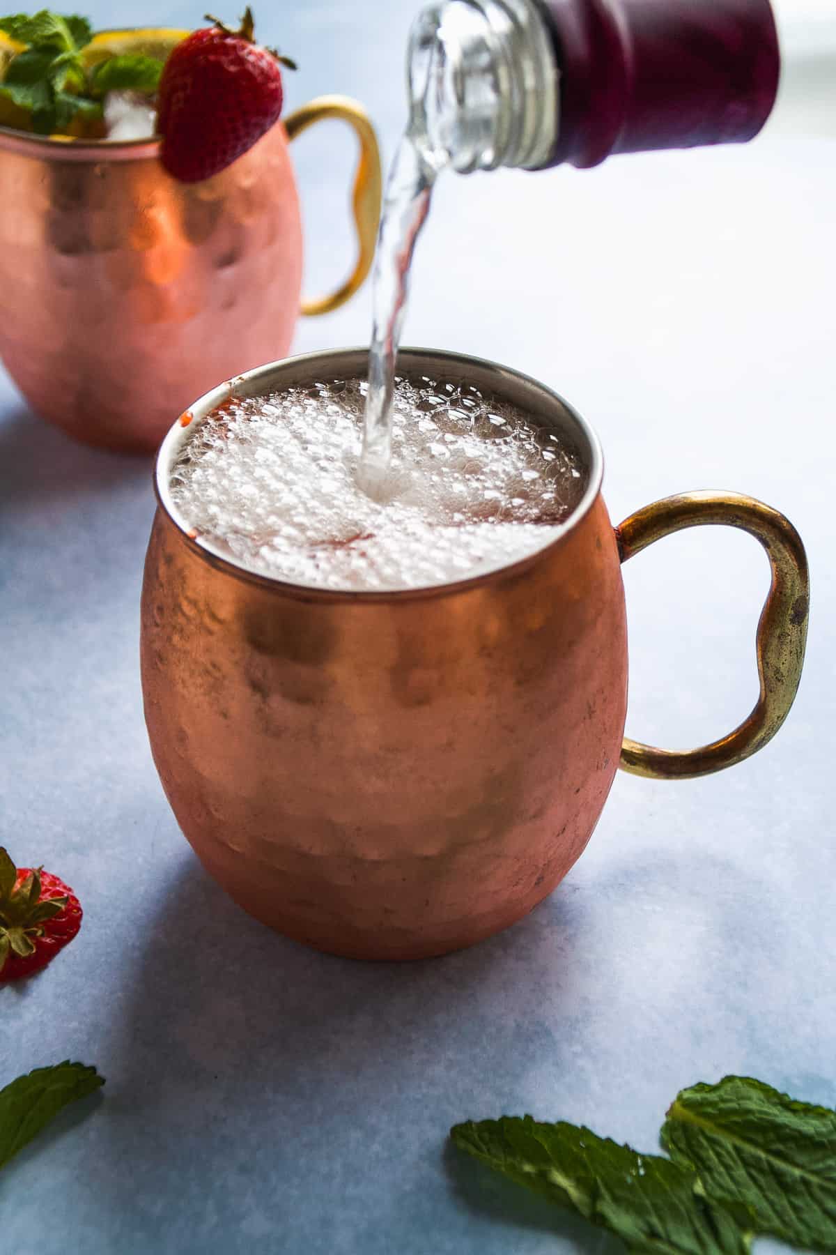 Ginger beer being poured into a copper mug creating bubbles on top.