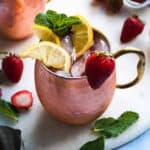 Kentucky mule drink in a copper mug with strawberries and lemon wedges on a white platter.