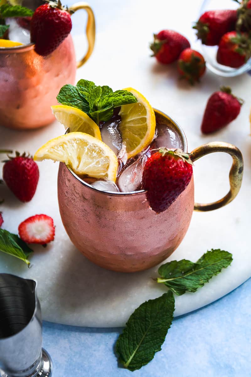 Kentucky mule in a copper mug with strawberries and lemon slices on top.