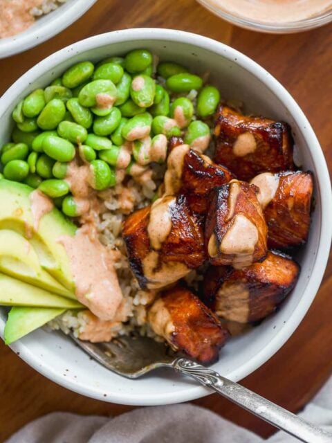Air fried teriyaki salmon bites with edamame and avocado in a white bowl with a fork.