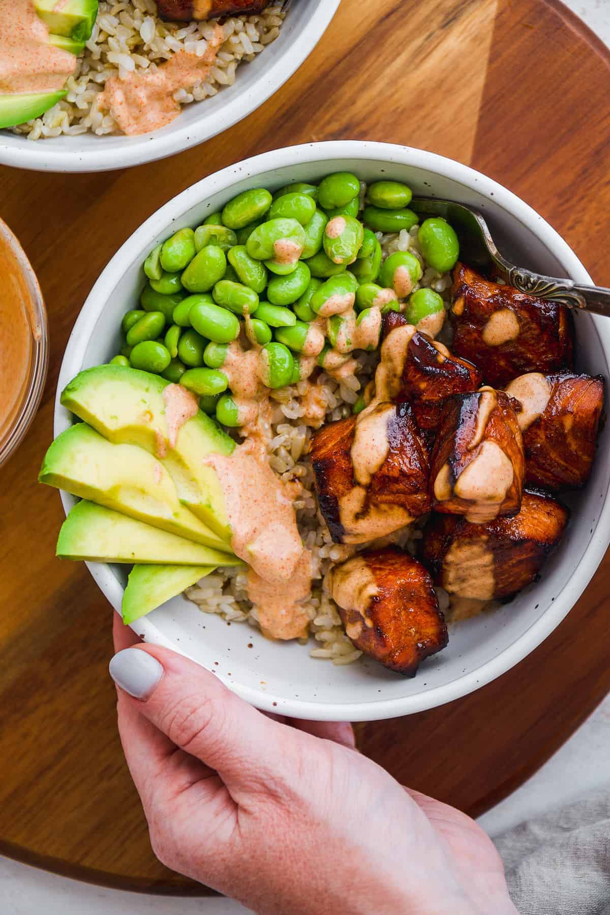 Rice bowl with teriyaki salmon bites, edamame, and avocado slices on top.