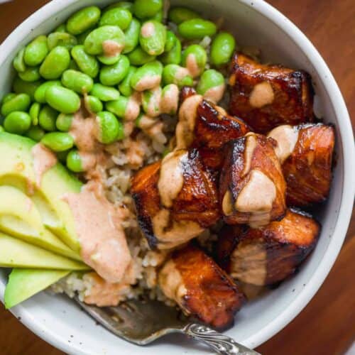 Overhead view of a bowl with teriayki air fried salmon bites and rice and greens.