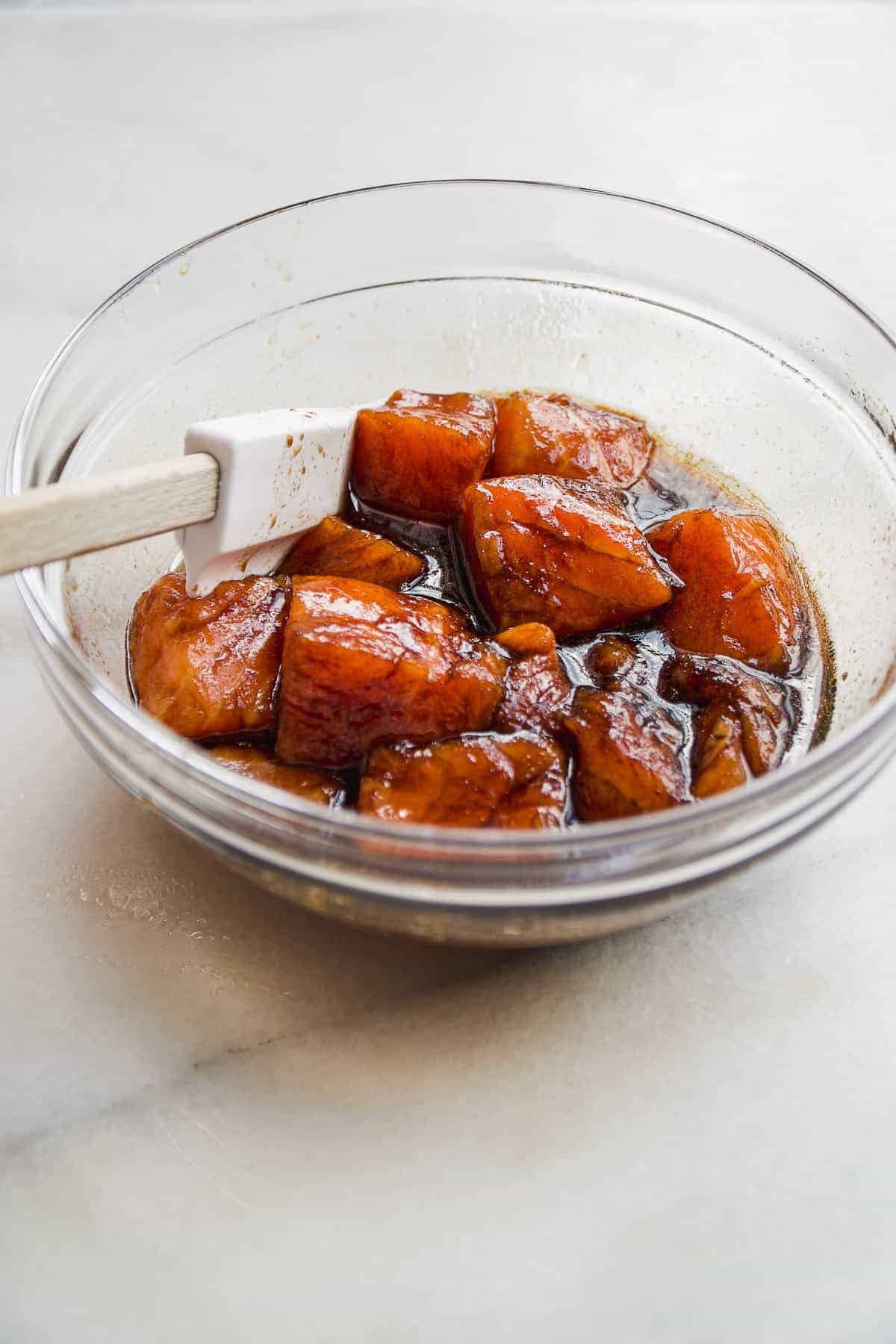 Chunks of salmon in a bowl marinading in teriyaki sauce.