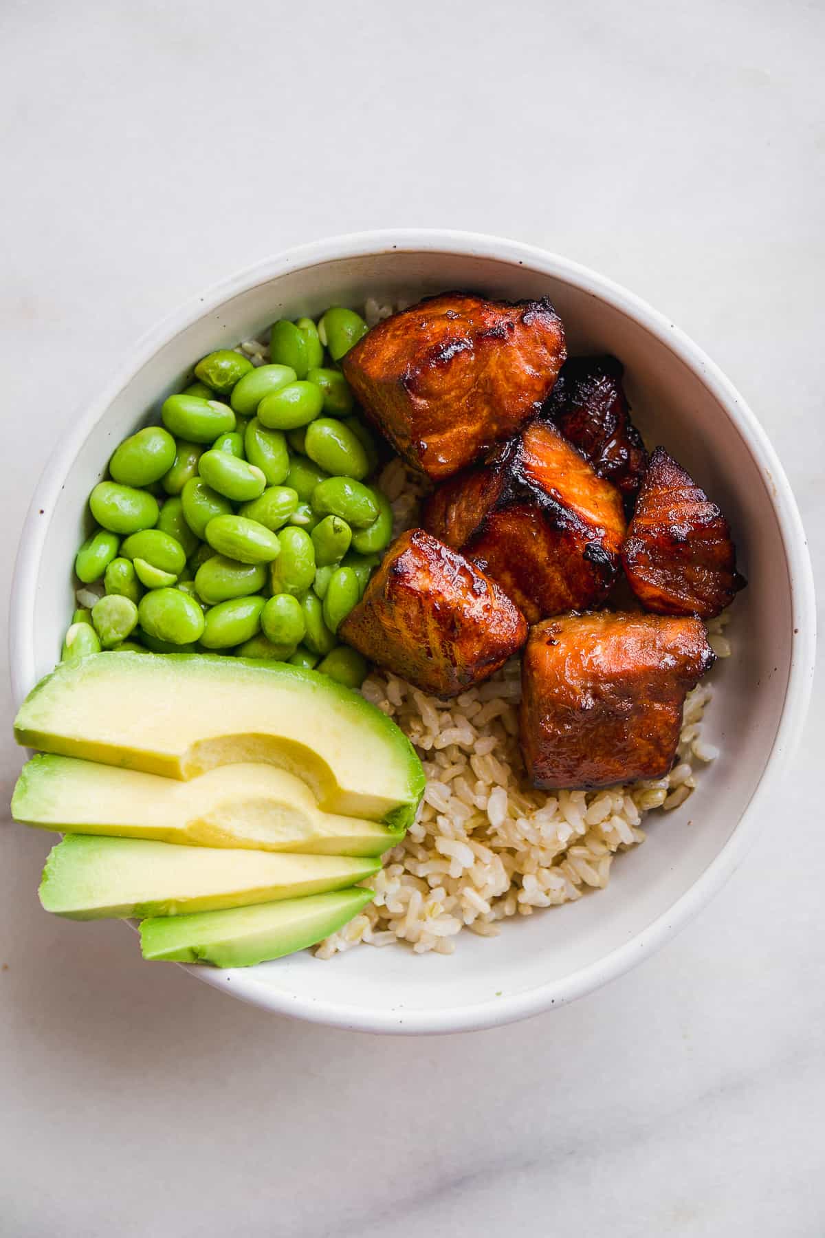 Overhead view of a bowl with air fried salmon bites with rice, edamame, and avocado slices.