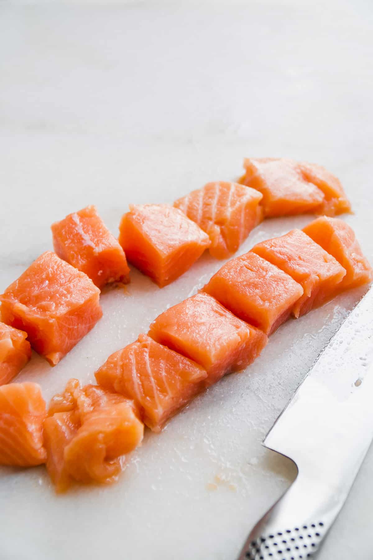Salmon filets cut into small chunks on a white marble slab.