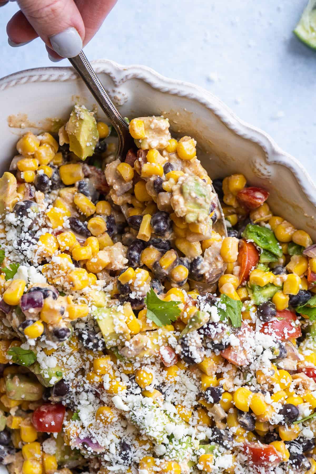 Person scooping mexican corn salad from a white serving dish.