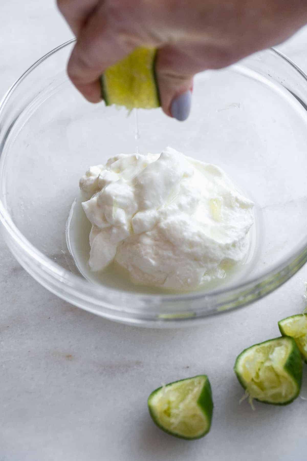 Person squeezing lime juice into a bowl with the greek yogurt. 