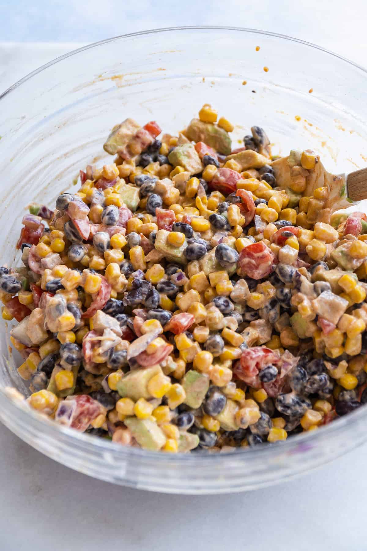 Creamy mexican corn salad tossed in the yogurt sauce in a clear bowl.