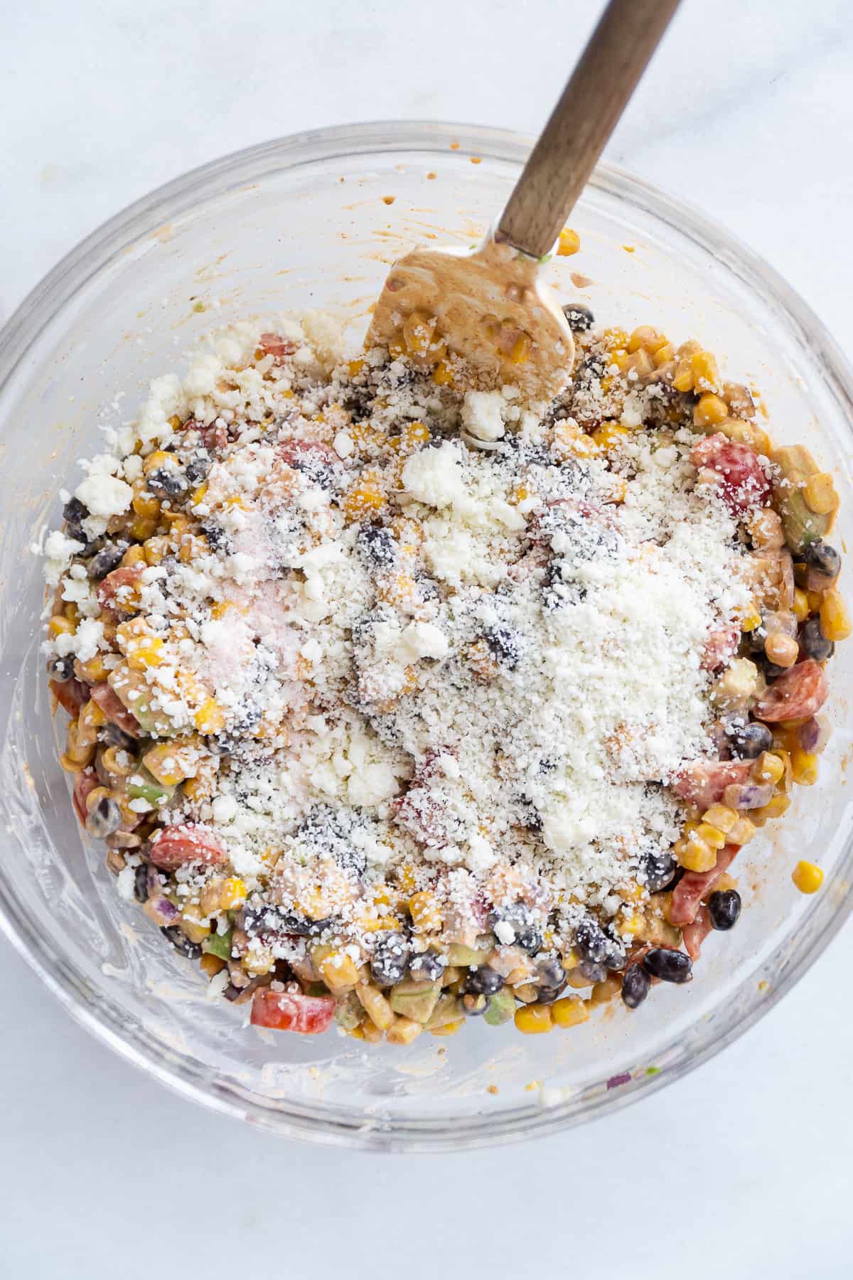 Overhead view of corn salad with cotija cheese sprinkled on top about to be mixed in.