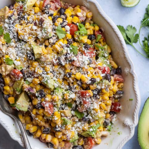 White dish with creamy corn salad with black beans and mexican cheese.