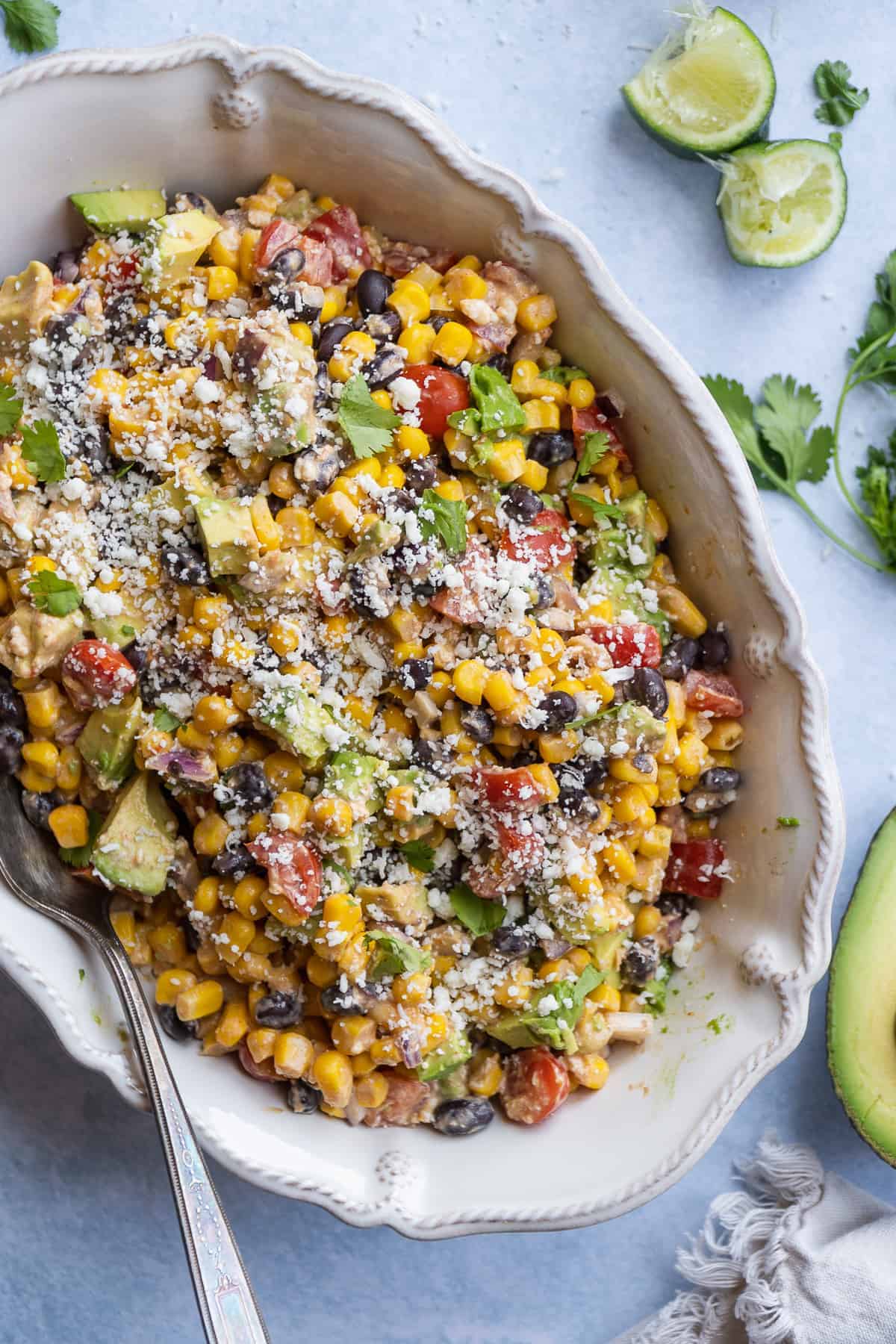 White dish with creamy corn salad with black beans and mexican cheese.