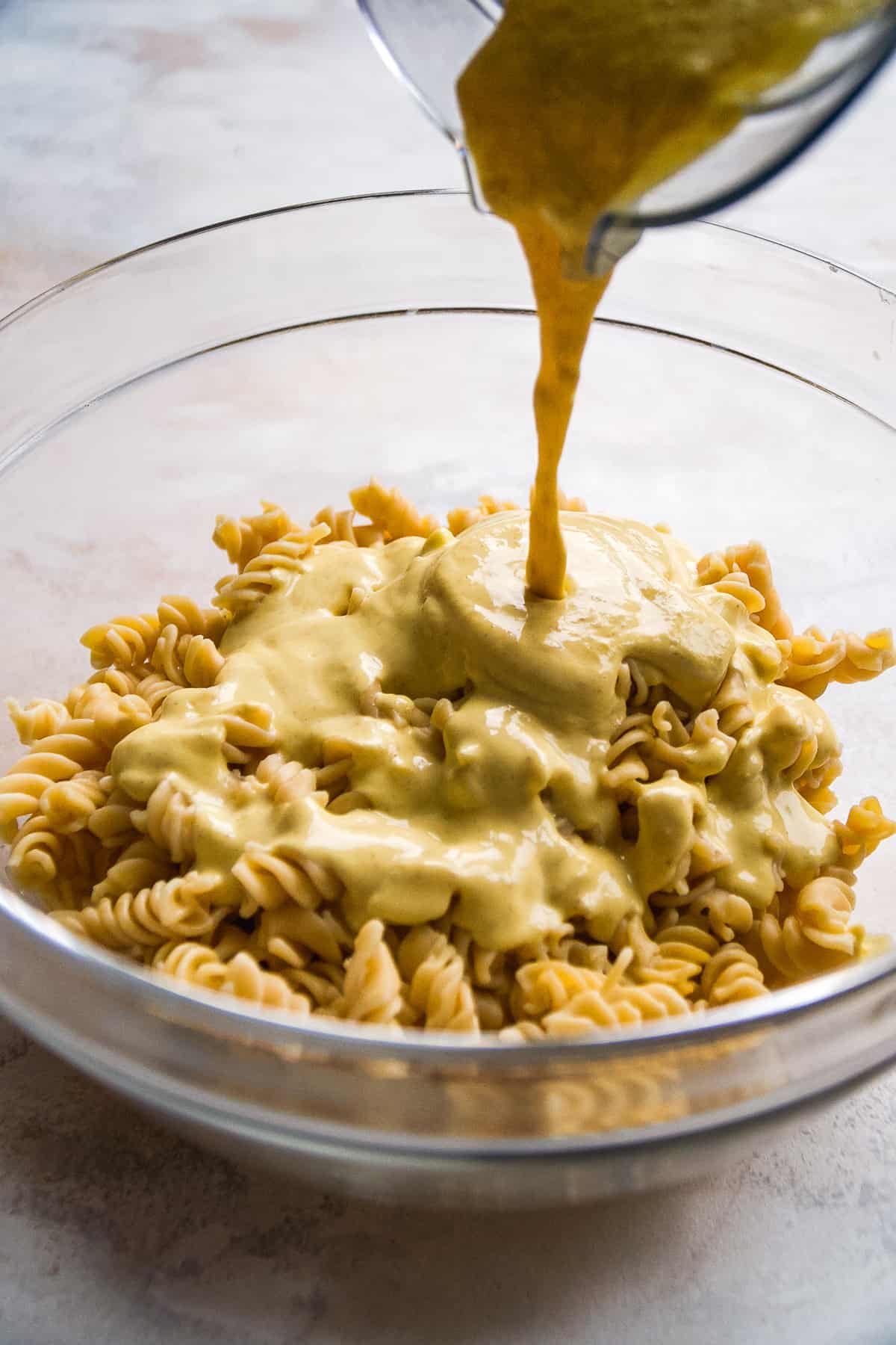 Deviled egg sauce being poured over pasta in a large bowl.