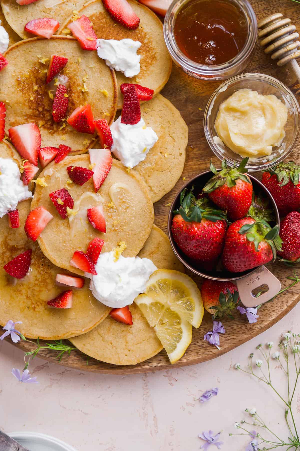 Lemon pancakes scattered on a wooden platter with strawberries.