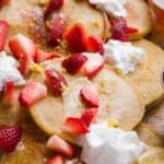 Lemon oat flour pancakes with strawberries on top scattered on a platter.