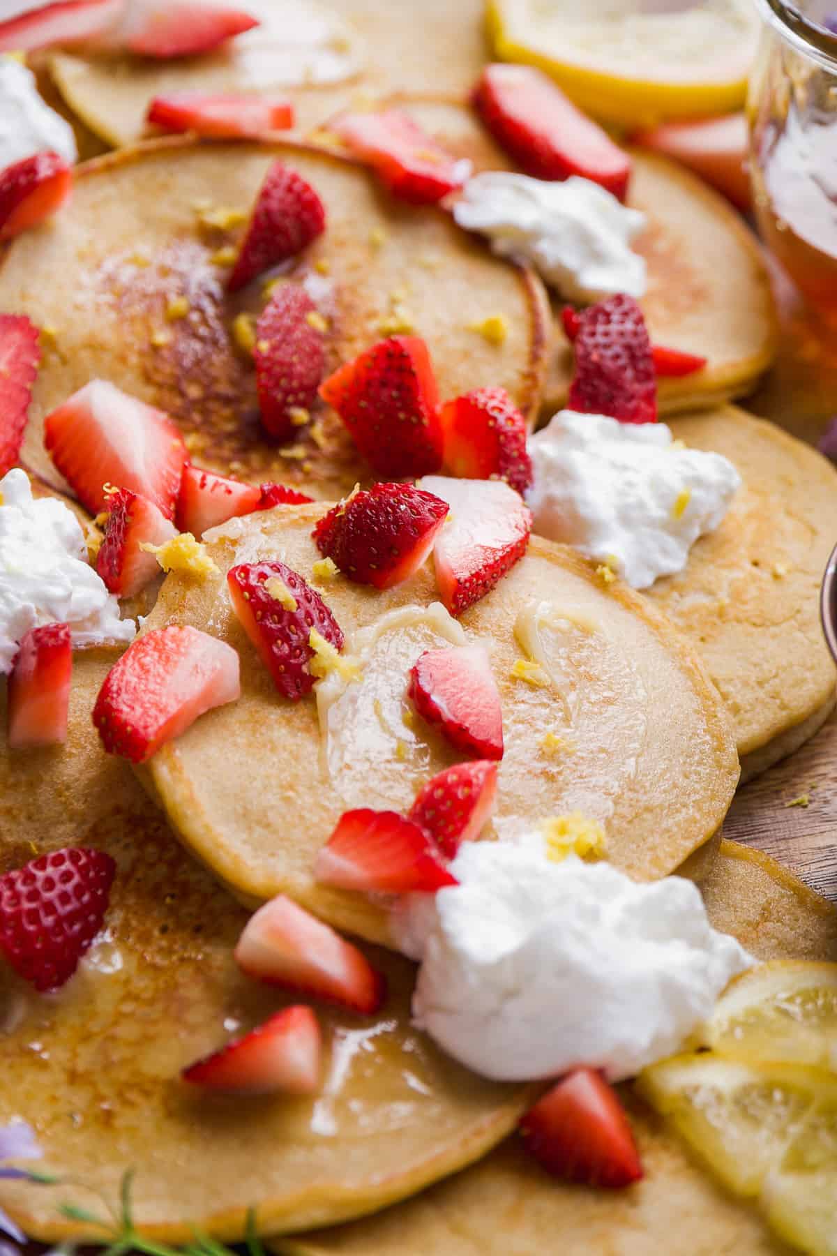 Lemon oat pancakes with sliced strawberries on top scattered on a platter.