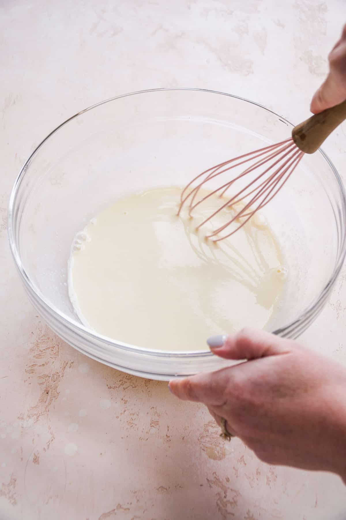 Person whisking together wet ingredients in a clear bowl.