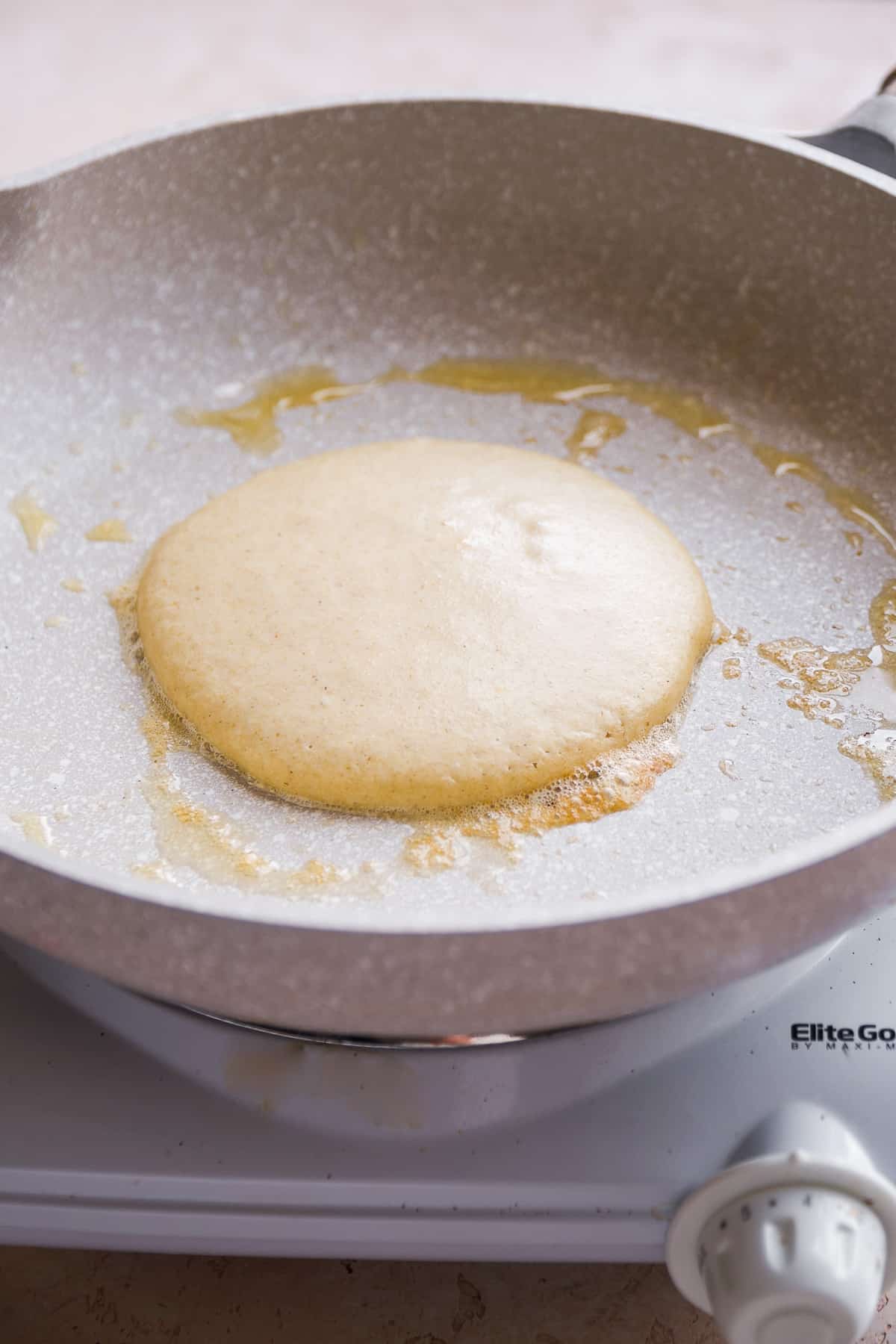 Pancake being cooked on a gray skillet.