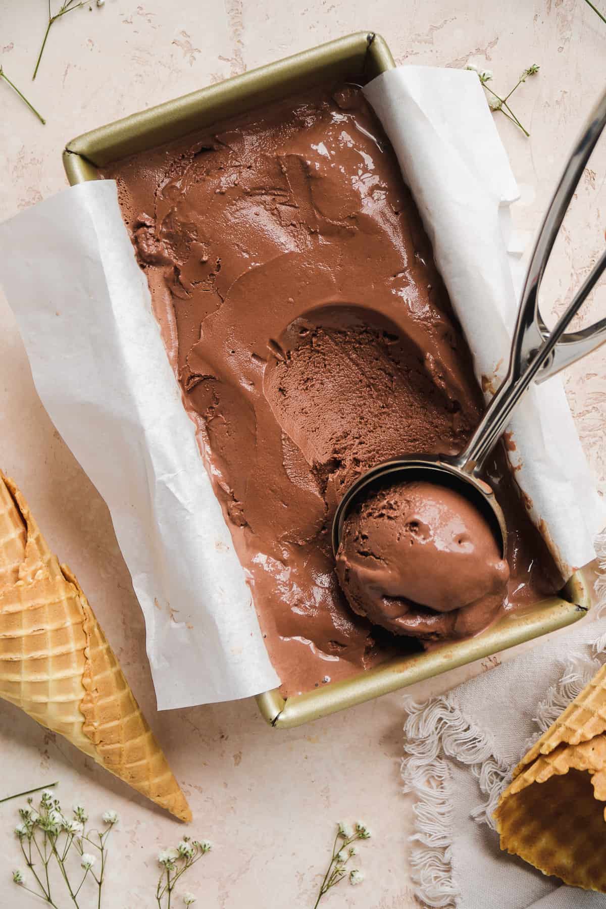 Overhead view of frozen chocolate yogurt in a rectangular pan with an ice cream scoop inside.