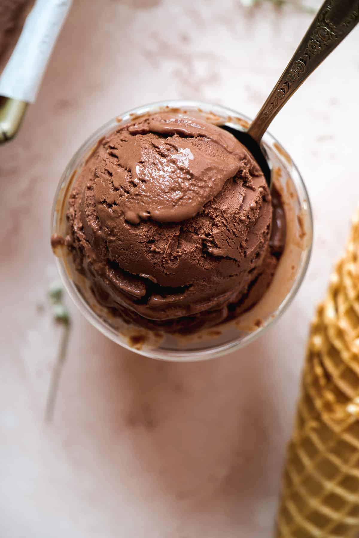 Overhead view of a scoop of frozen chocolate yogurt in a cup with a spoon inside.