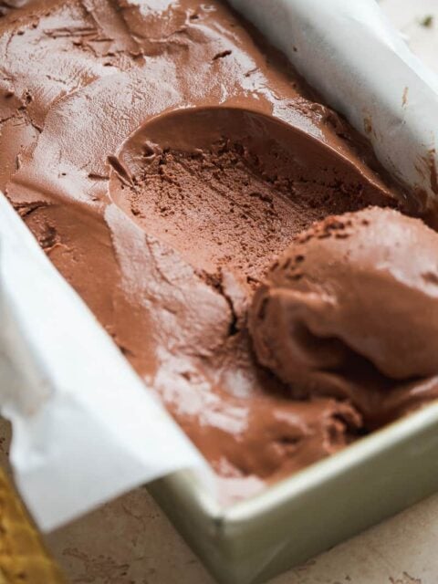 Frozen chocolate yogurt in a rectangular dish with parchment paper with a scoop taken out.