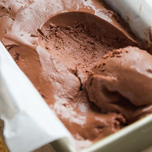 Frozen chocolate yogurt in a rectangular dish with parchment paper with a scoop taken out.