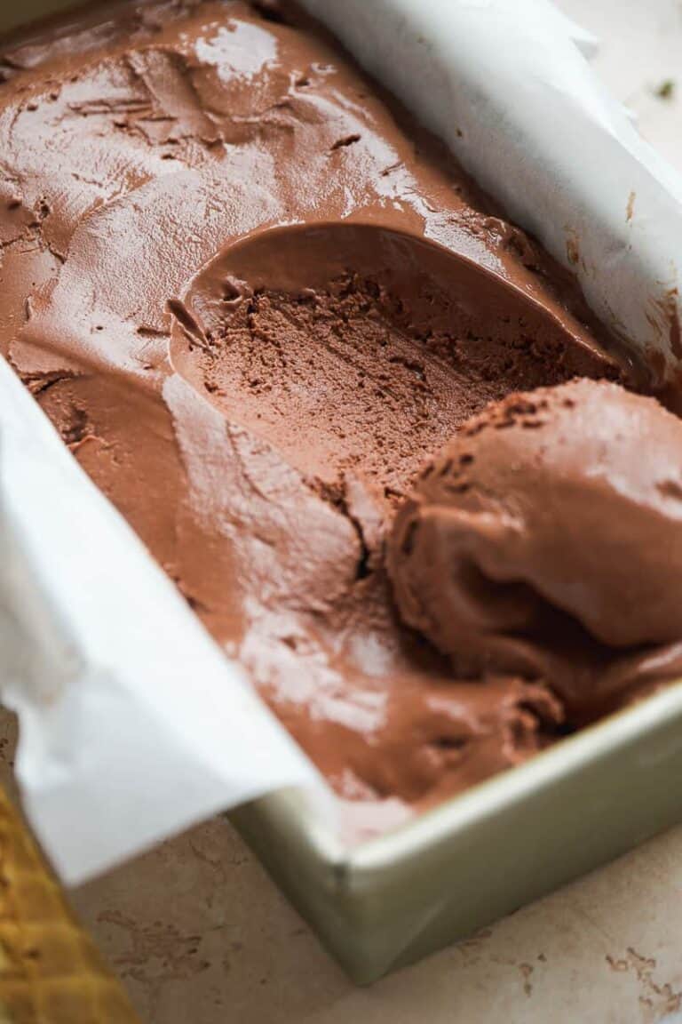 Frozen chocolate yogurt in a rectangular dish with parchment paper with a scoop taken out.