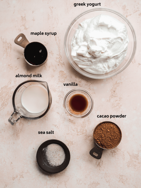 Chocolate frozen greek yogurt ingredients scattered on a pink surface.