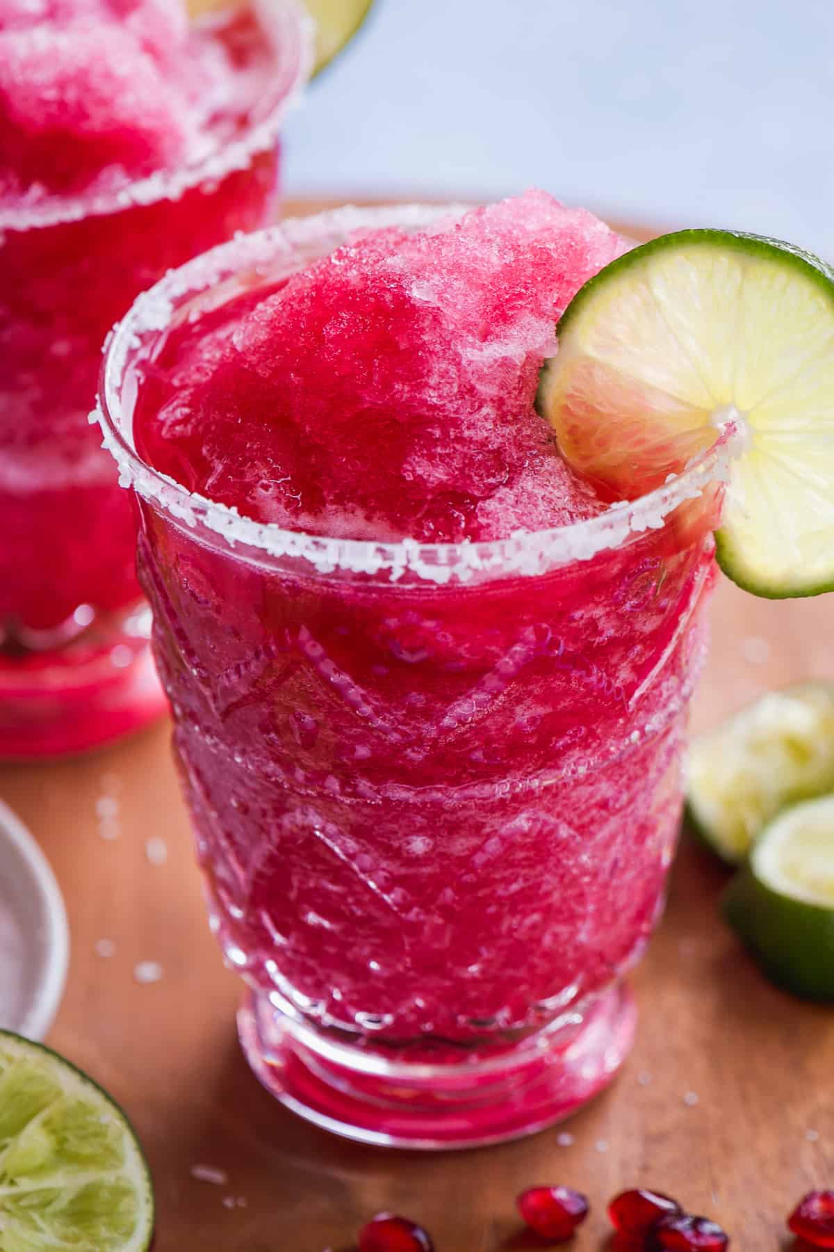 Up close view of a pink margarita mocktail in a glass with a lime on the rim.