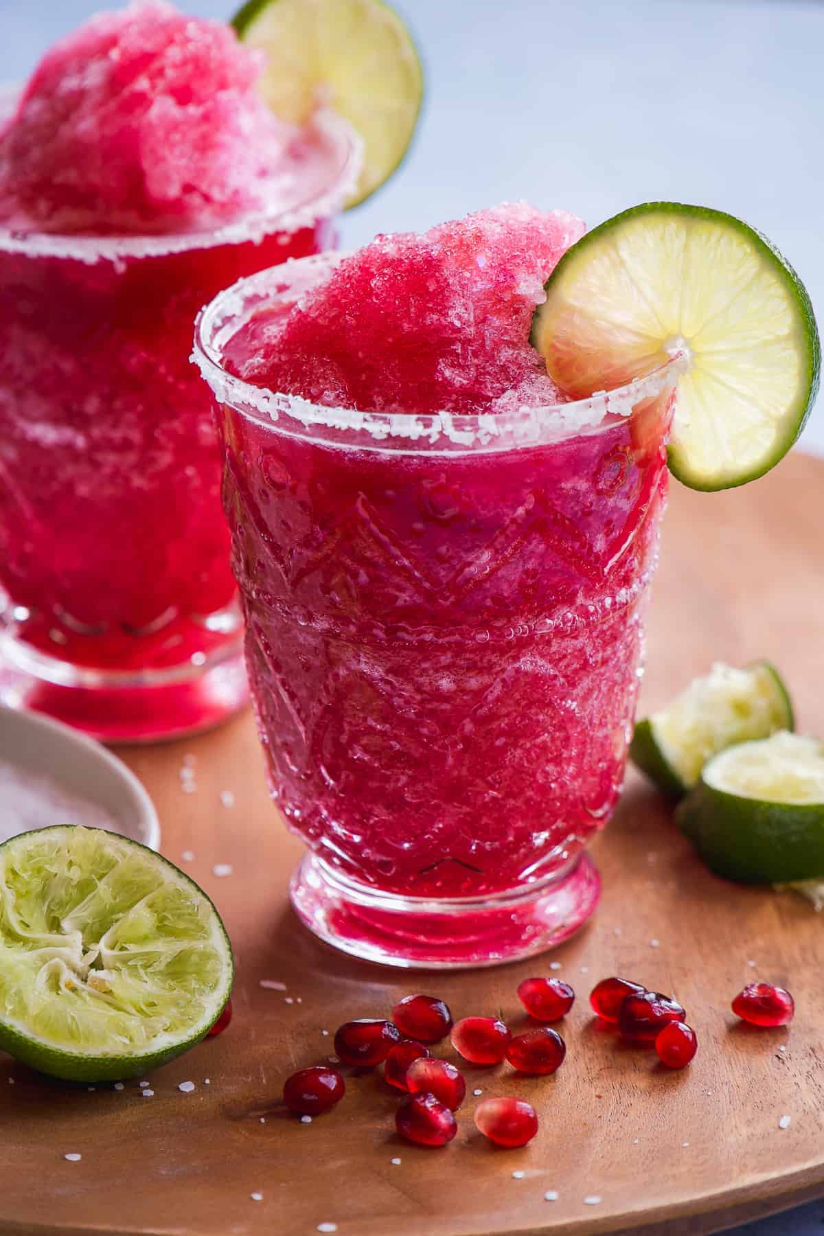 Frozen pomegranate margarita mocktail in a glass with a lime wedge on the rim.