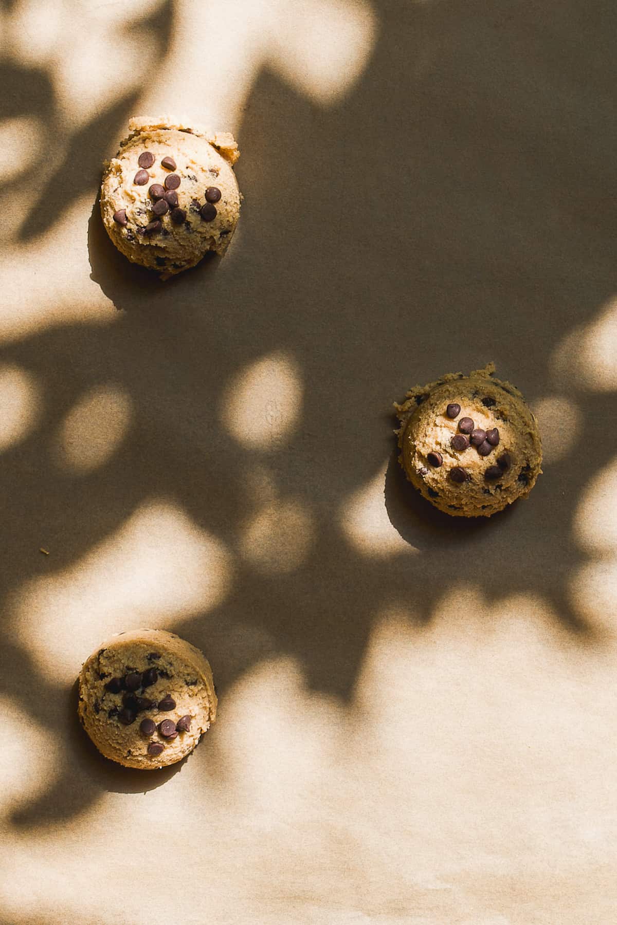 Three oatmeal cookie dough balls on a baking sheet with parchment paper.