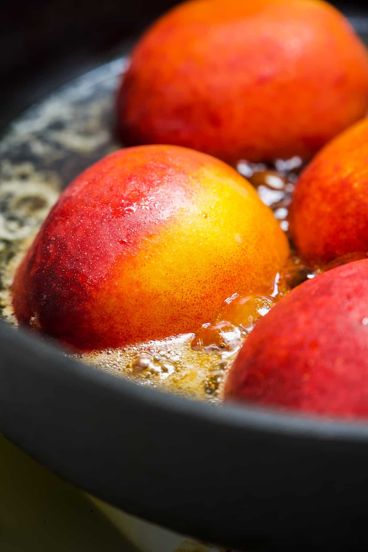 Peaches cooking in sugar and butter in a black pan.