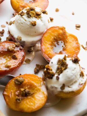Caramelized peaches with ice cream and crumble on top on a marble surface.