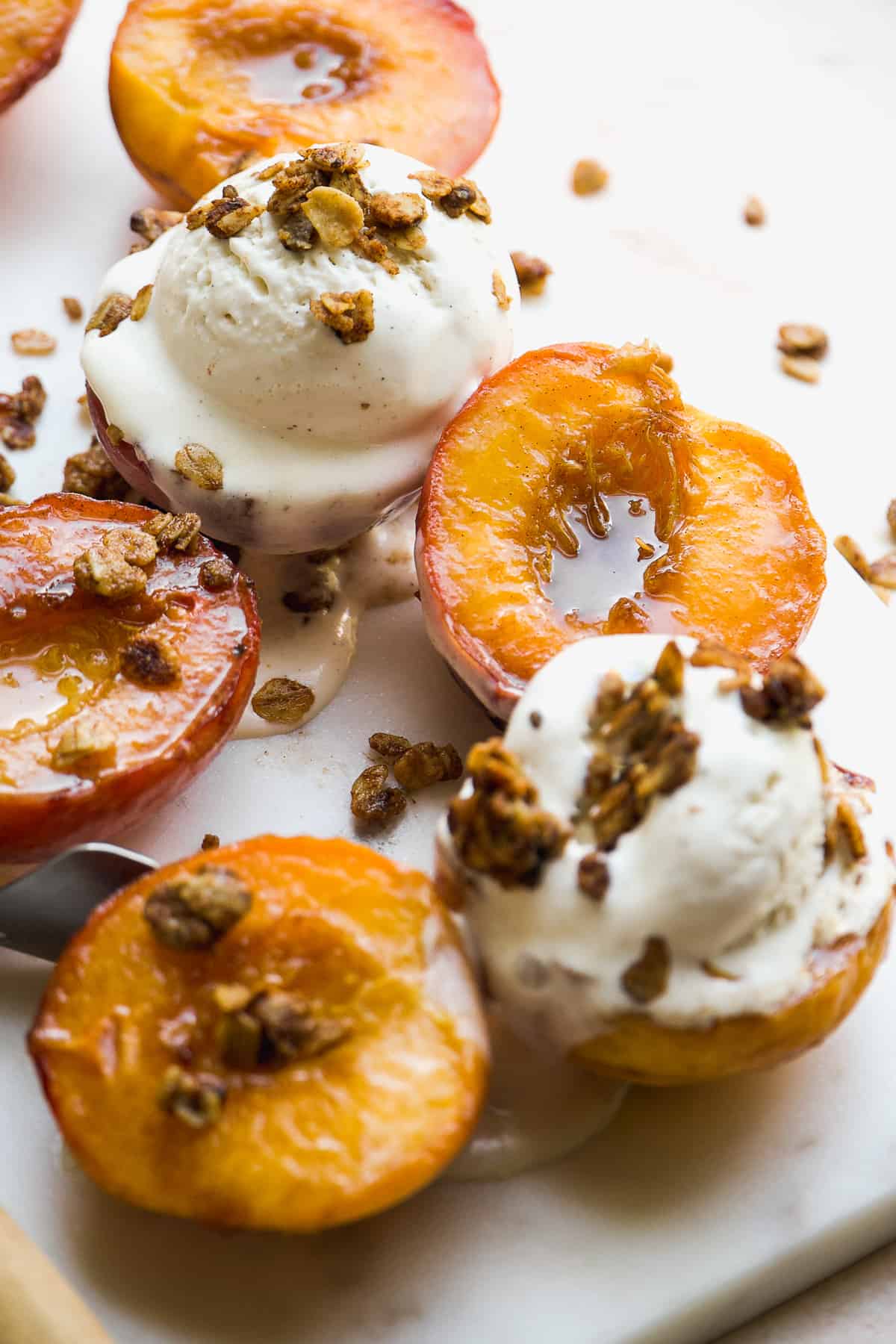 Caramelized peaches with ice cream and crumble on top on a marble surface.