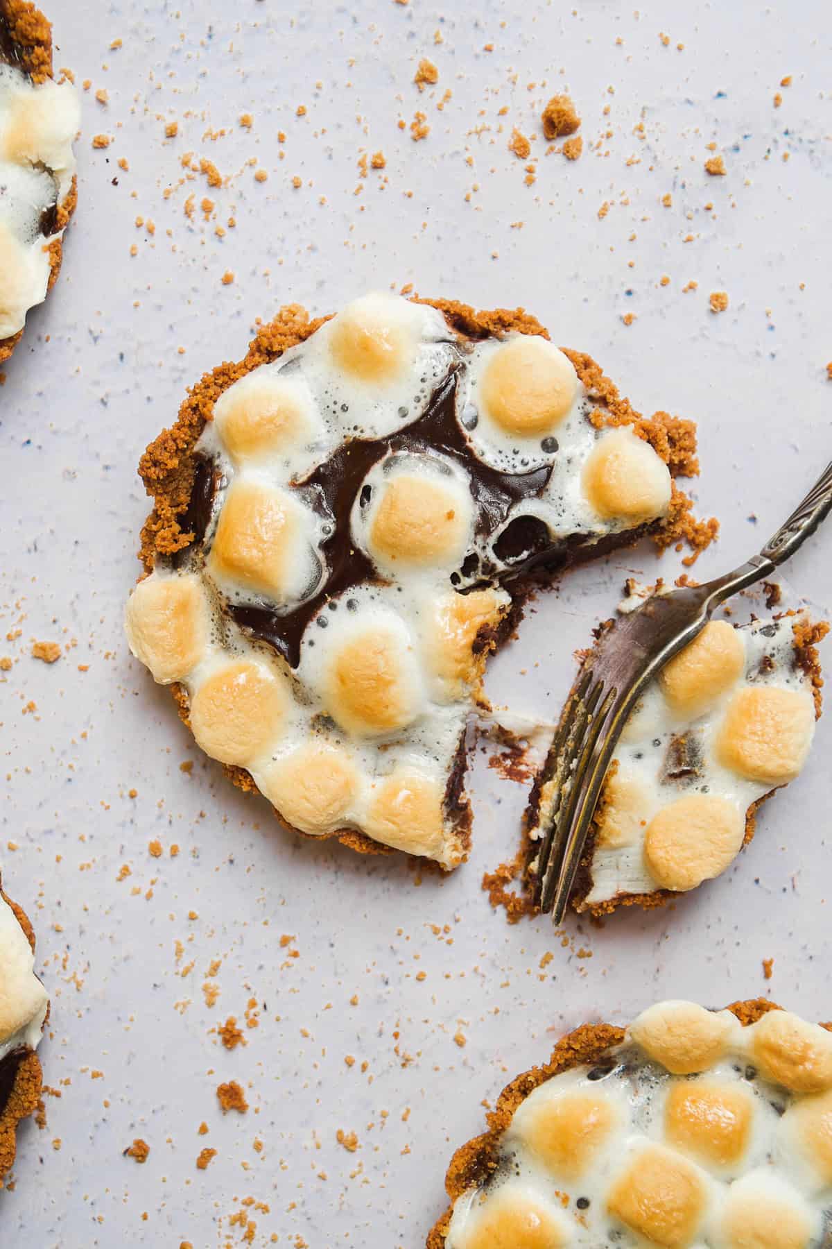 Mini s'mores pie on a light surface with a fork taking a bite out of one.