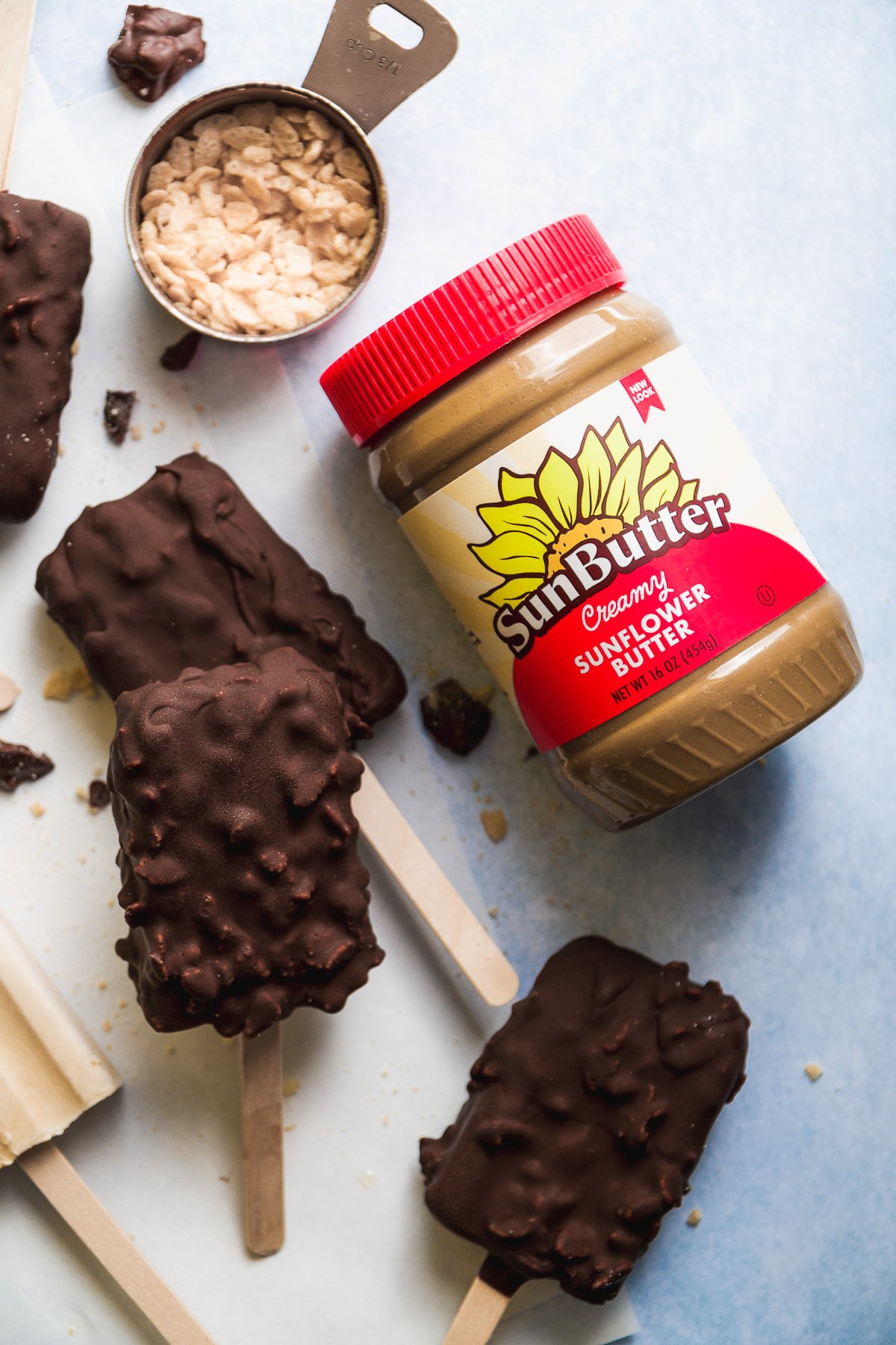 Chocolate frozen yogurt bars spread out on parchment paper with a jar of SunButter next to it.