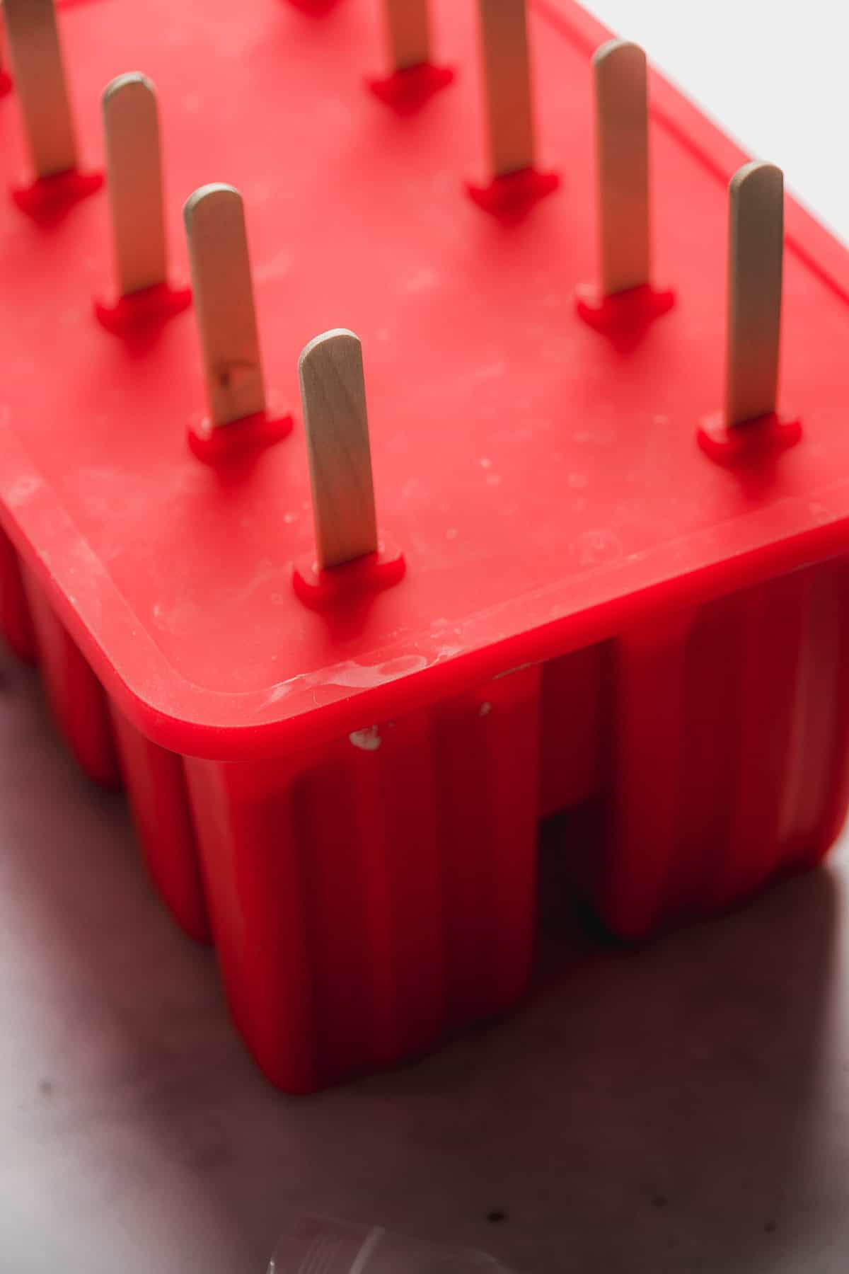 Red popsicle mold with sticks inside.