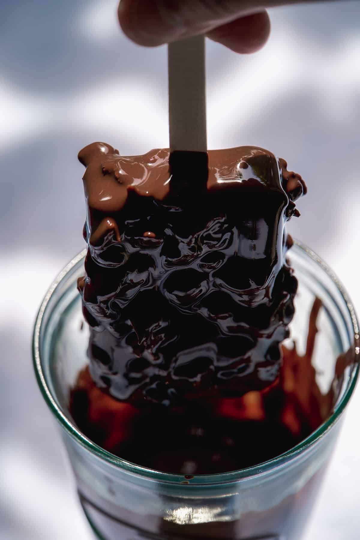 Person holding up a popsicle after being dipped in melted chocolate.