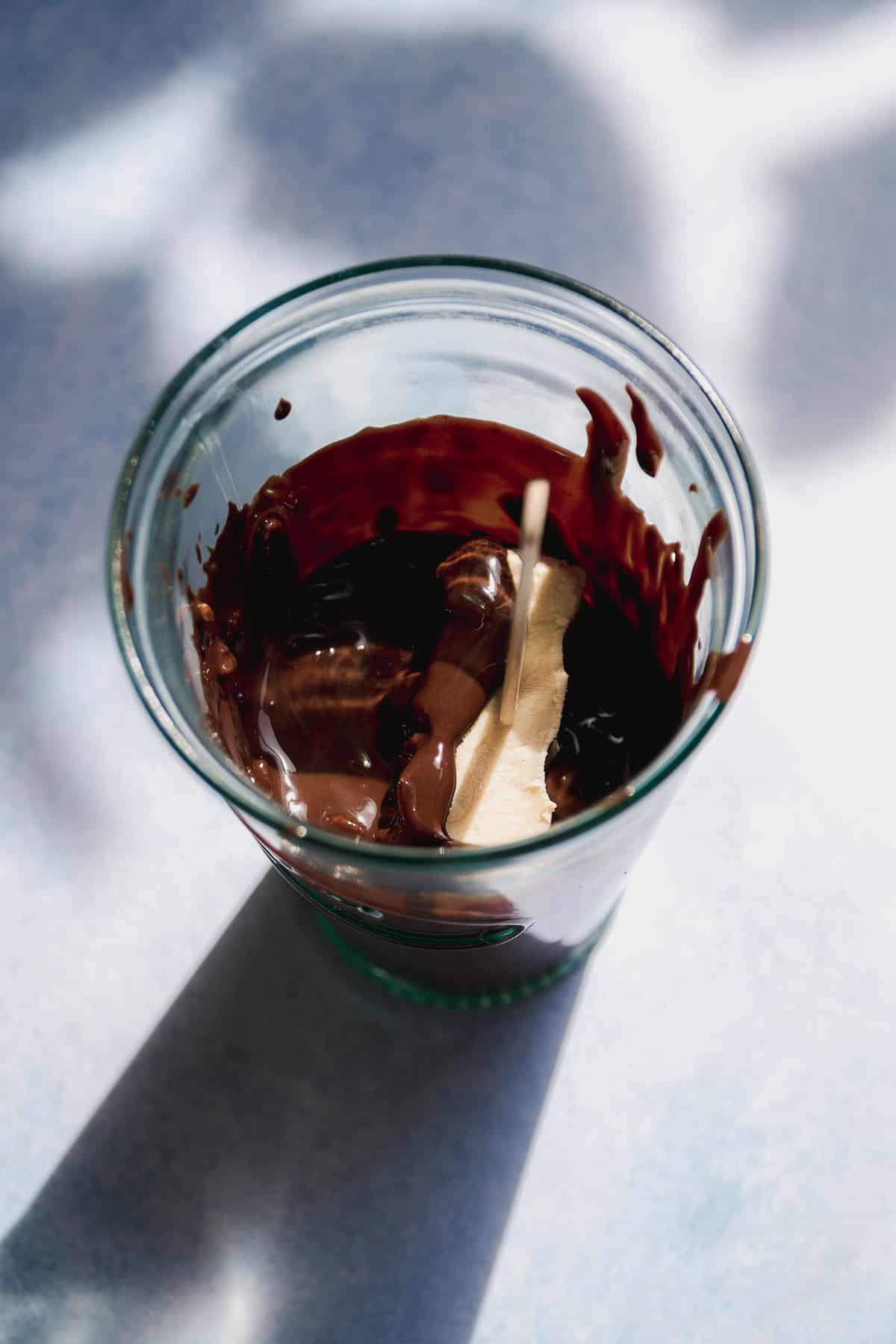 Frozen yogurt bar submerged into a glass of melted chocolate.