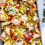 Greek nachos in a baking pan on a blue surface.
